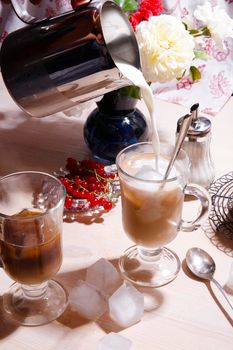 Summer breakfast with iced coffee, fresh red currant berries and milk pouring into a glass, selective focus