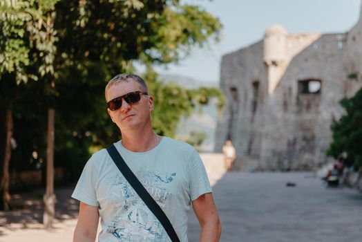 A handsome young man standing and smiling happily in the background of urban buildings. Forty years old caucasian tourist man outdoor near old city buildings - summer holiday.