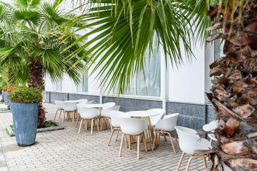 Street cafe with white chairs, green foliage around. Without people, tourism, travel