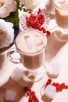 A cup of iced coffee and bouquet of white roses and red currant berries on white table in rustic kitchen, summer morning concept, selective focus, bright light with shadows.