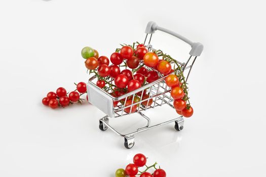 Mini shopping cart full with cherry tomatos on white background. Copy space
