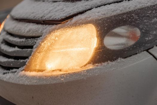 snow covered headlight of silver civiliian car at winter morning, close-up