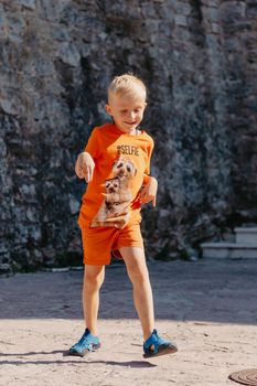 Kid's outdoor activity. Smile toddler boy wearing a orange shorts Jumping, running and having fun in a backyard on a sunny hot summer day. Full length of energetic little boy in stylish casual outfit jumping outdoor