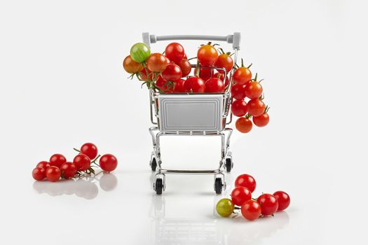 Mini shopping cart full with cherry tomatos on white background. Copy space