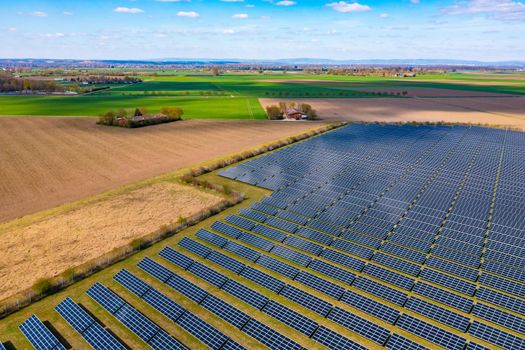 A drone view of a solar park with photovoltaic panels next to fields and a farm