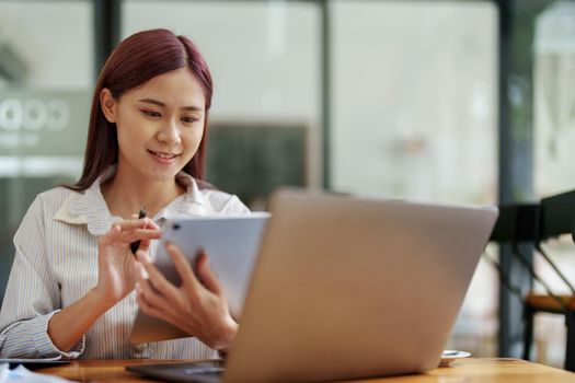 Portrait of an Asian female employee using a tablet computer to work to gather information and analyze marketing plans and investment budgets to increase company profits.