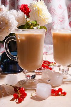 Two glasses of iced coffee and bouquet of white roses and red currant berries on white table in rustic kitchen, summer morning concept, selective focus, bright light with shadows.