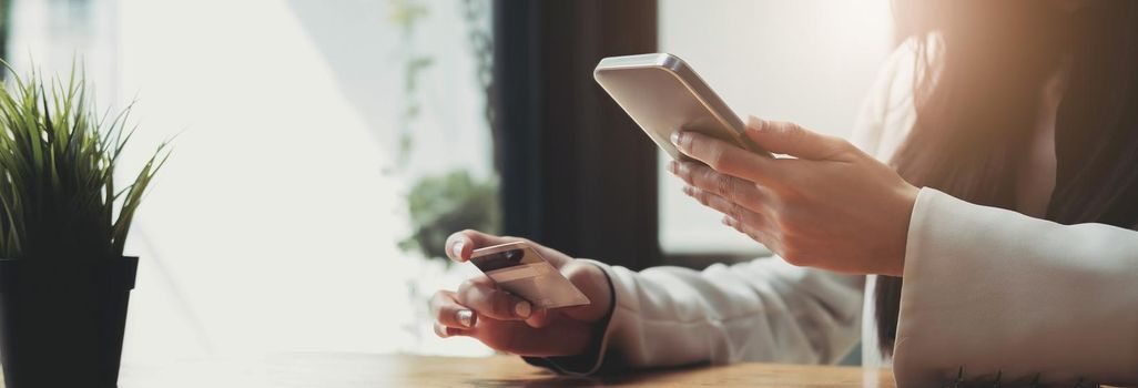 Hands holding credit card and using mobile smart phone at cafe