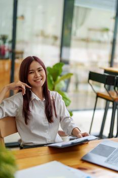 Portrait of a businesswoman holding documents and using computers to analyze budget work and make marketing plans to meet the needs of office clients.