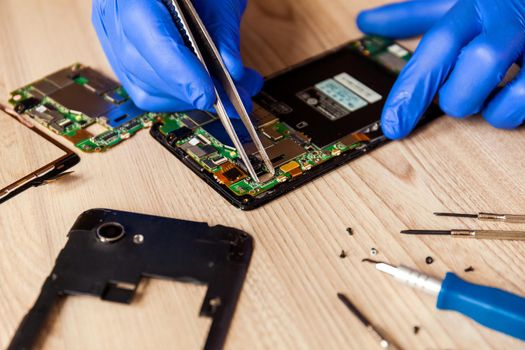 The technician repairing the smartphone's motherboard in the workshop on the table. Concept of mobile phone, electronic, upgrade and technology.
