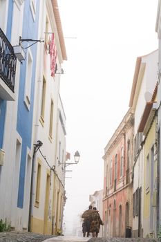 A street in a Portuguese town with colorful houses, a paved road and a couple walking along it during the day