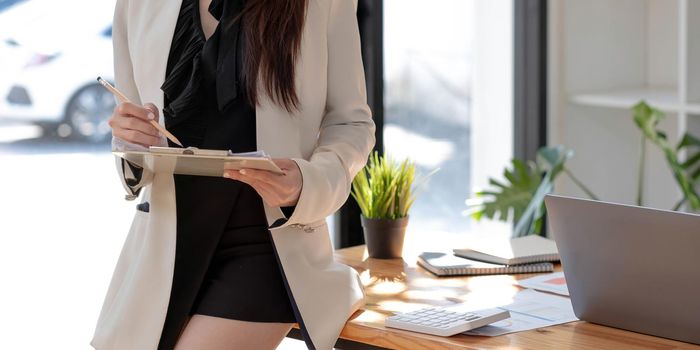 asian woman in casual wear holdng clipboard, smiling while standing in modern office room