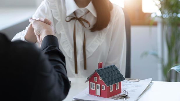 The real estate agent is explaining the house style to the clients who come to contact to see the house design and the purchase agreement. Within a modern office.