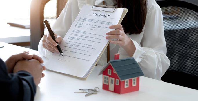 The real estate agent is explaining the house style to the clients who come to contact to see the house design and the purchase agreement. Within a modern office.