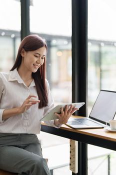 Portrait of an Asian female employee using a tablet computer to work to gather information and analyze marketing plans and investment budgets to increase company profits.