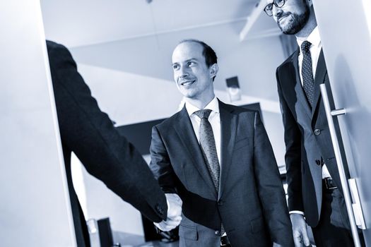 Group of confident business people greeting with a handshake at business meeting in modern office. Closing the deal agreement by shaking hands. Greyscale blue toned image.