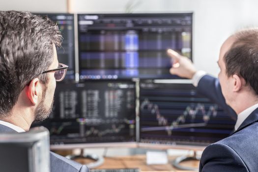 Businessmen trading stocks online. Stock brokers looking at graphs, indexes and numbers on multiple computer screens. Colleagues in discussion in traders office. Business success concept.