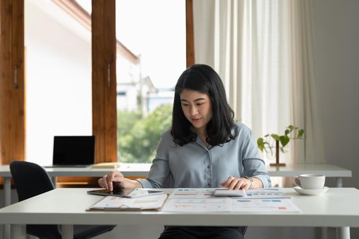 Charming asian businesswoman sitting working on laptop for paperwork in office.