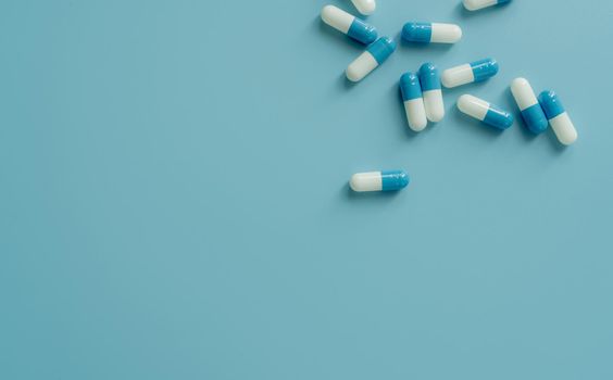 Top view blue-white antibiotic capsule pills on blue background. Prescription drug. Antibiotic drug resistance. Pharmaceutical industry. Pharmaceutical care. Pharmaceutics concept. Antimicrobial drug.