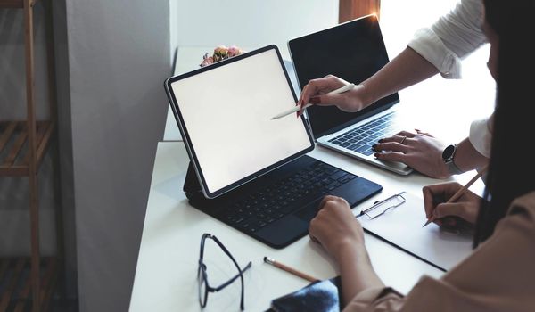 Two businesswomen meet in a meeting room for a business consultation, using a laptop computer and tablet. mockup of a laptop with a blank screen.