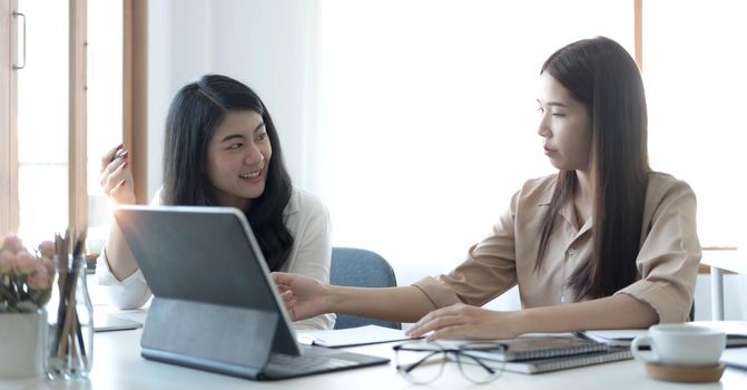 Two young Asian businesswoman discuss investment project working and planning strategy. Business people talking together with laptop computer at office..