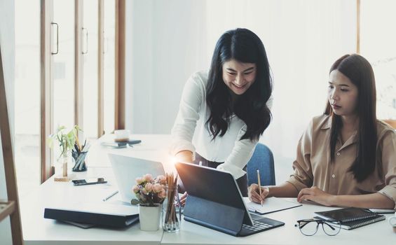 Two young Asian businesswoman discuss investment project working and planning strategy. Business people talking together with laptop computer at office..