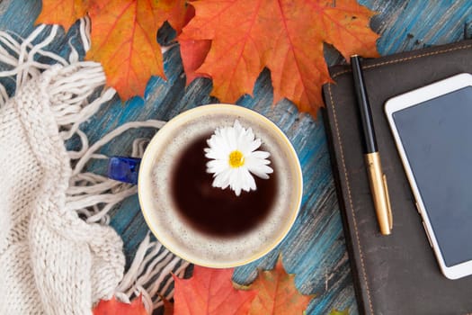 Autumn layout, a cup of coffee with flower, orange leaves, notebook, a knitted sweater, a smartphone