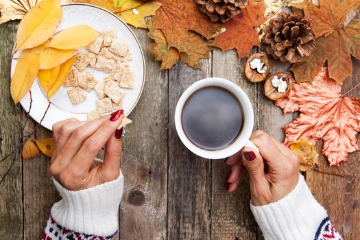 cozy autumn breakfast - coffee and sweet chips. Female hands are holding a cup of coffee. Wooden table and autumn leaves