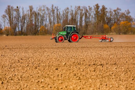 In the background, in front of a row of trees, a farmer is plowing a field with a tractor