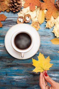 Hot coffee on a wooden table, in the hand of a girl - autumn yellow maple leaf.