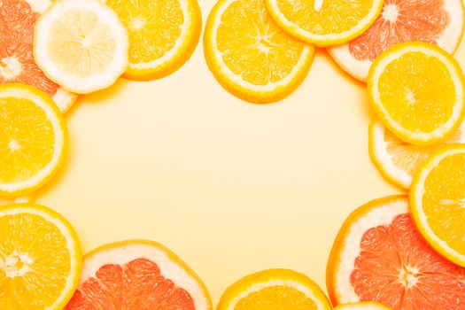 Flat lay slices of orange, grapefruit and lemon formed a frame on a yellow background. Bright summer citrus composition for your text.