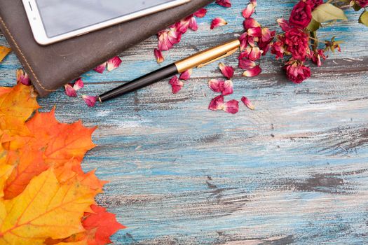 Autumn layout on a blue vintage background with smartphone, notebook, pen, dry roses and empty place for text