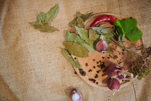 View from above. Pickling dry fragrance ingredients on a wooden board: garlic cloves, peppercorns, chili pepper, fresh dill, blackberry leaves and bay leaf on a kitchen table with a linen tablecloth