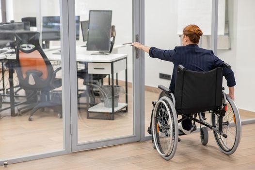 Red-haired caucasian woman in a wheelchair trying to open the door in the office