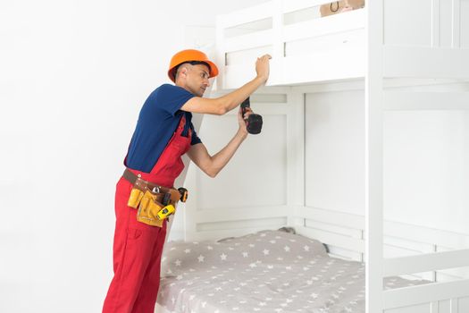 A man with instructions for assembling furniture is going to assemble a children's white wooden crib in a children's bedroom