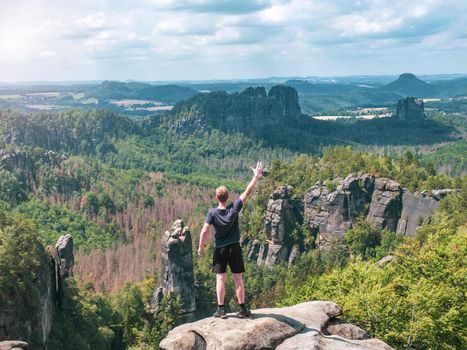 Hiker shouts greetings into valley bellow Carolafelsen rock, Grossen Dom and jagged mountains Schrammsteine and Falkenstein