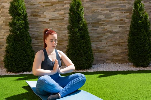 young and beautiful woman, practising meditation in the garden in the open air, relaxation exercises, doing the lotus posture. concept of health and well-being. natural outdoor light.