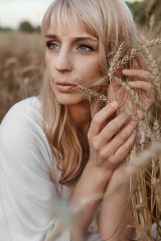 A blonde woman in a long white dress walks in a wheat field. The concept of a wedding and walking in nature.