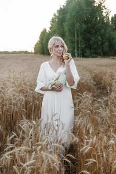 A blonde woman in a long white dress walks in a wheat field. The concept of a wedding and walking in nature.