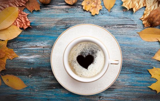 Autumn layout, a cup of coffee with a heart inside the foam, orange and golden leaves on vintage blue wooden background