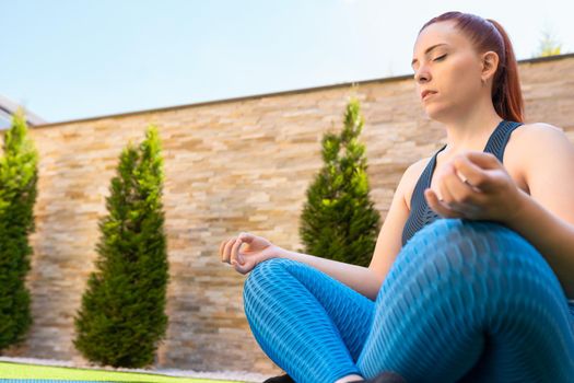 view from below young woman doing yoga, in lotus position, on a mat in the garden. girl doing meditation and breathing exercises. concept of health and well-being. natural light in the garden.