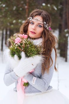 Beautiful bride in a white dress with a bouquet in a snow-covered winter forest. Portrait of the bride in nature.Beautiful bride in a white dress with a bouquet in a snow-covered winter forest. Portrait of the bride in nature.