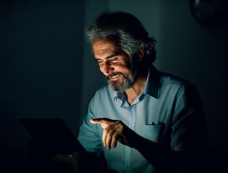 Portrait of a senior businessman with tablet or laptop working late at night in office