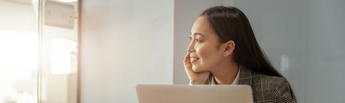 Smiling business asian woman working in office use computer and looking away. Blurred background