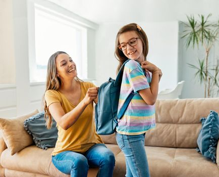 Mother helping daughter to get ready for school, helping her with backpack and books,hugging and leaving home