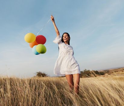Happy young girl running with ballons through meadow grass