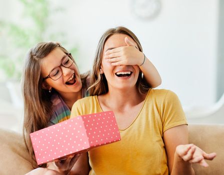 Daughter surprises her mother with present covering her eyes with her hand on mother's day or birthday at home