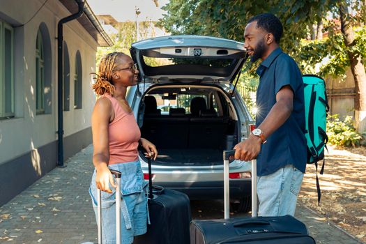 African american couple loading baggage in trunk, leaving together on holiday vacation. Man and woman preparing to travel on adventure trip with luggage and suitcase by vehicle.