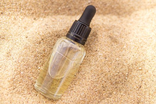 Cosmetic serum for the skin in a glass bottle. A bottle with a pipette on a sandy beach by the sea. Essences for skin care on a sandy background. The concept of natural cosmetics and SPA products.