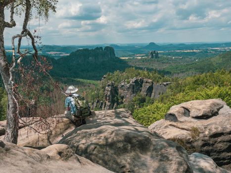 Schmilka - Germany, July 06, 2022: Tourist with camera is taking photos behind the Schrammsteine rock massif, Saxon Switzerland, Germany. View from the Carolafelsen viewpoint